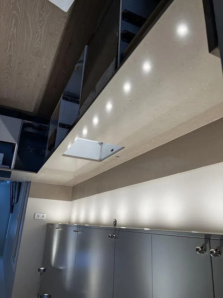 Köksbänkskiva i greige Silestone Coral Clay, polerad, längs väggen med infälld induktionshäll och uppvikt stänkkant i ett kök i Ängelholm.