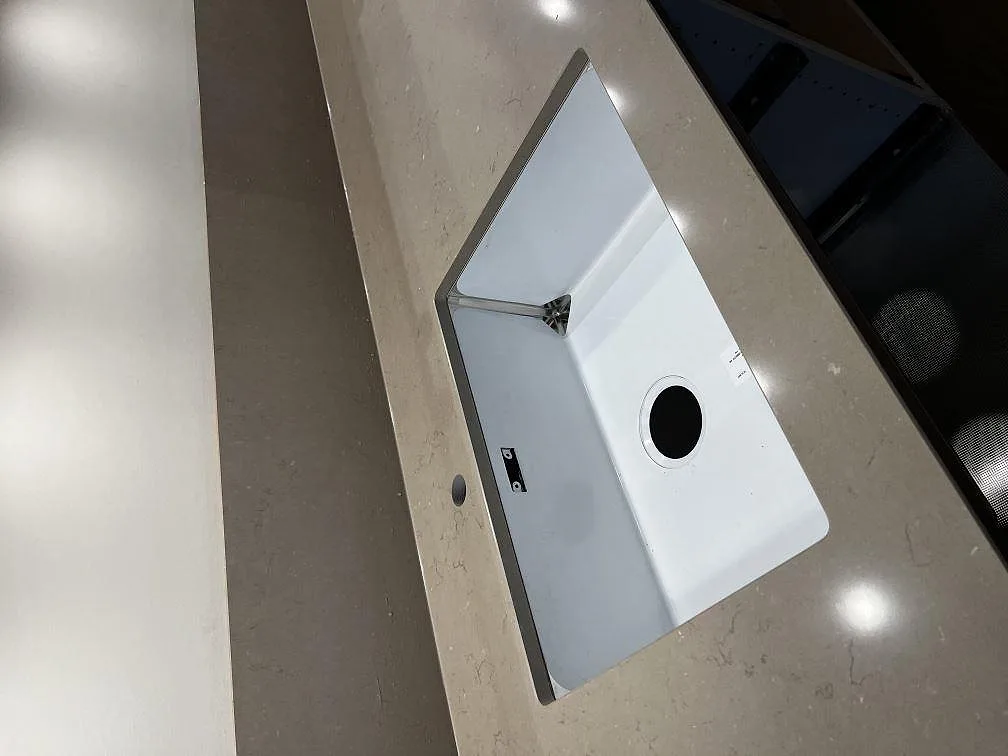 Underlimmad vit enkelho med urtag för avlopp i en polerad bänkskiva av Silestone Coral Clay i ett kök i Ängelholm.
