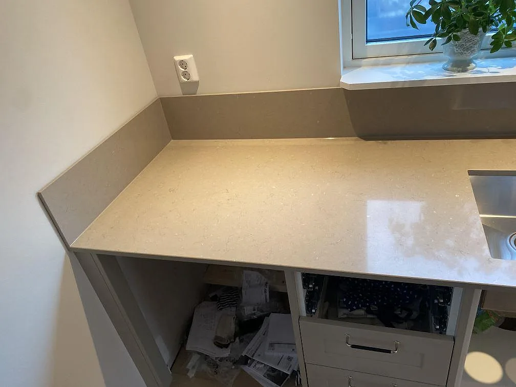 Hörn av köksbänk i Silestone Coral Clay med uppvikt stänkkant och eluttag, polerad greige kvartskomposit i ett kök i Alingsås under montering.
