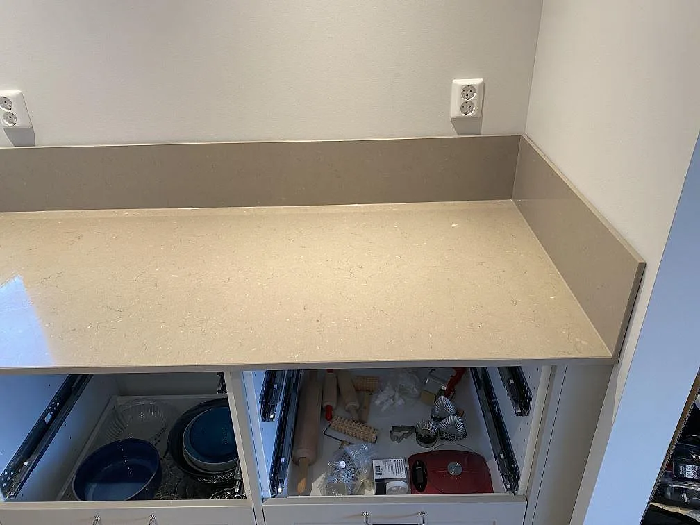 Polerad Silestone Coral Clay köksbänkskiva med uppvikt stänkkant sedd ovanifrån över öppna lådor i ett kök i Alingsås.