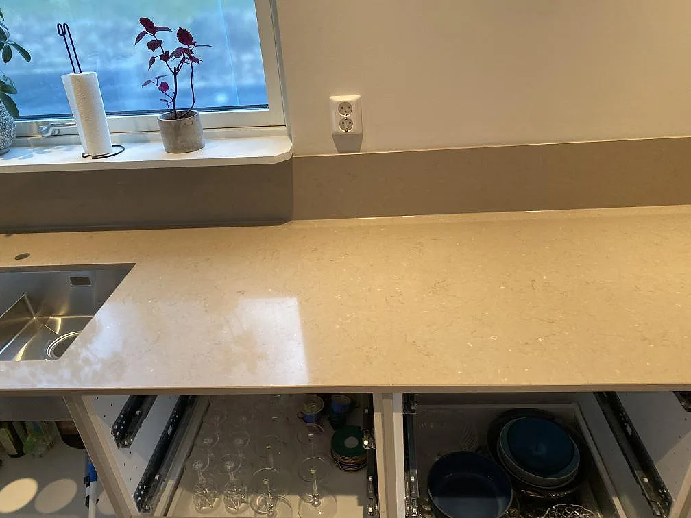 Köksbänkskiva i Silestone Coral Clay med uppvikt stänkkant i samma sten och underlimmad rostfri diskho vid fönstret i ett kök i Alingsås.