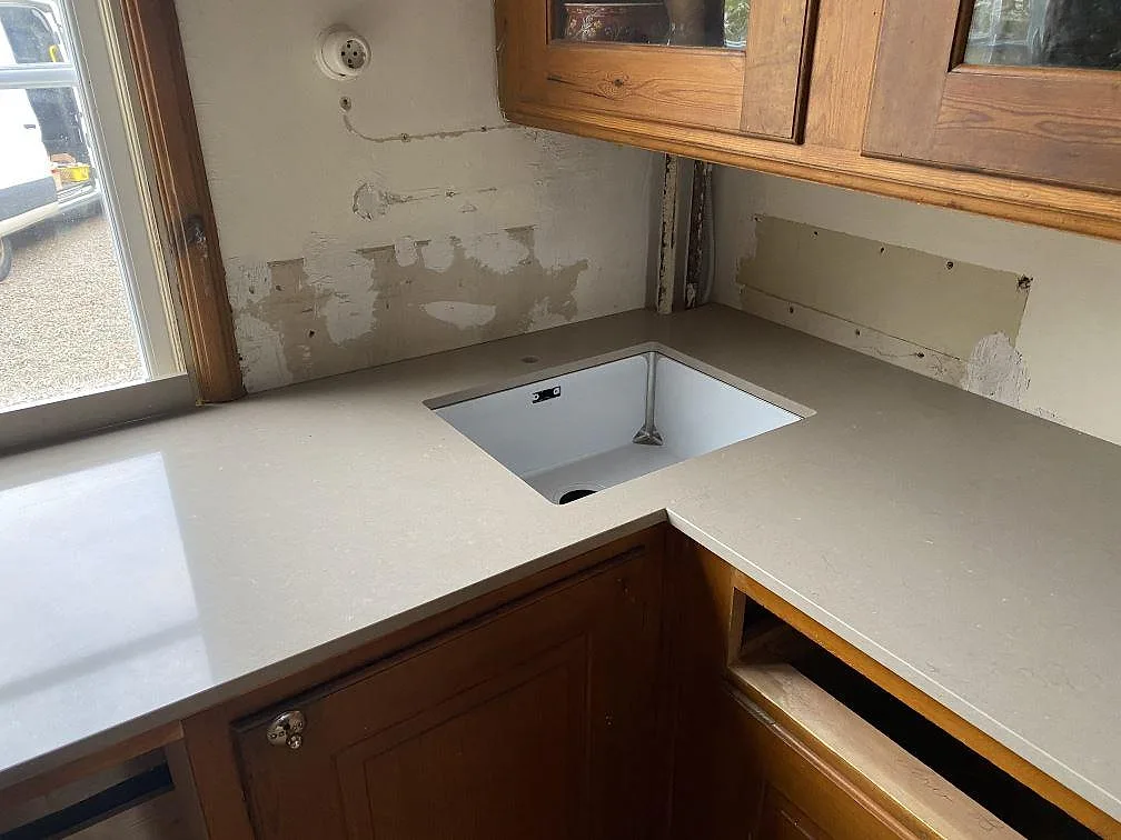 Underlimmad diskho infälld i köksbänkskiva av Silestone Coral Clay vid fönstret, vägg utan stänkskydd ännu, i ett kök under montering i Alingsås.