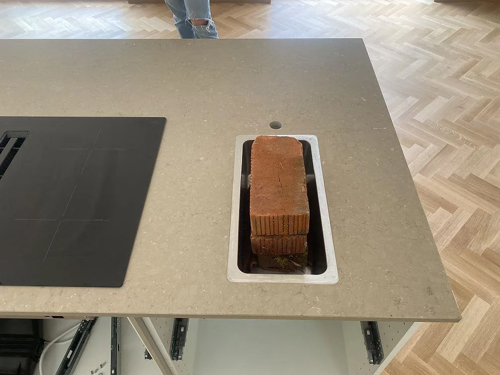 Detalj av polerad Silestone Coral Clay på köksö i Båstad, med svart häll och öppning under pågående montering.