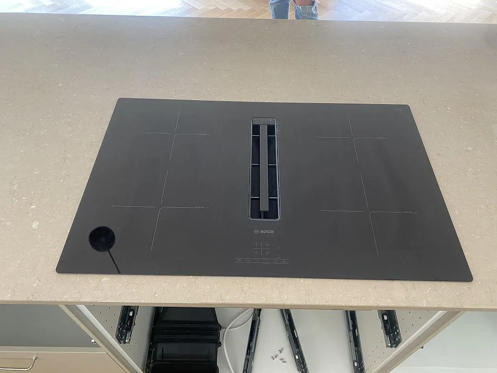 Detalj av polerad Silestone Coral Clay bänkskiva på köksö i Båstad med svart induktionshäll monterad i stenen.