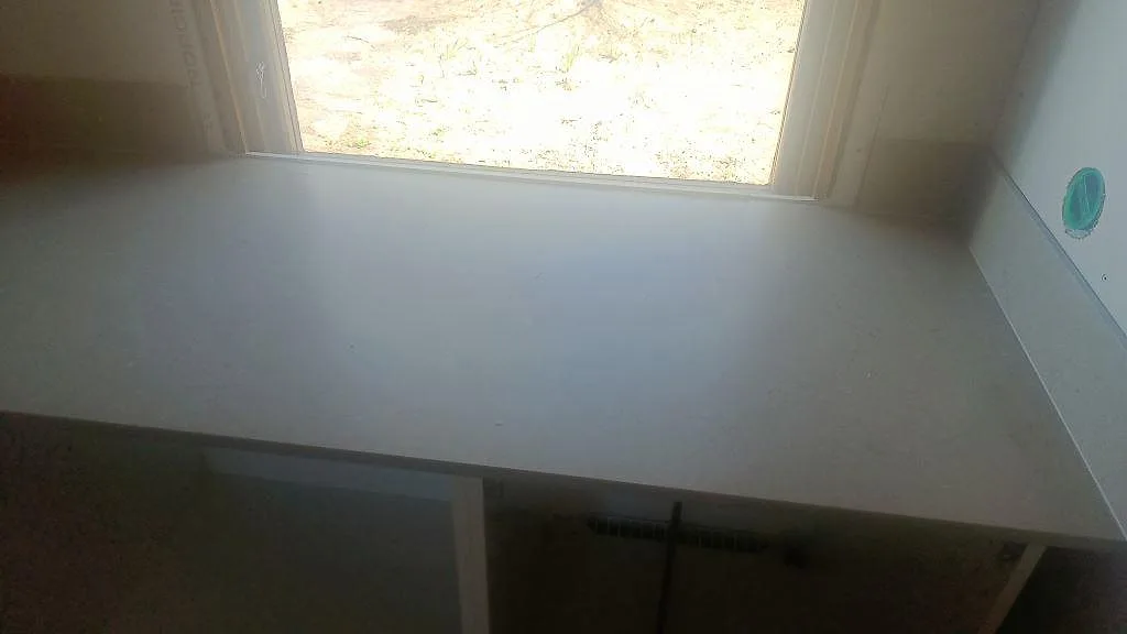 Rak bänkyta i matt Silestone Coral Clay komposit under fönster i ett kök under montering i Båstad.