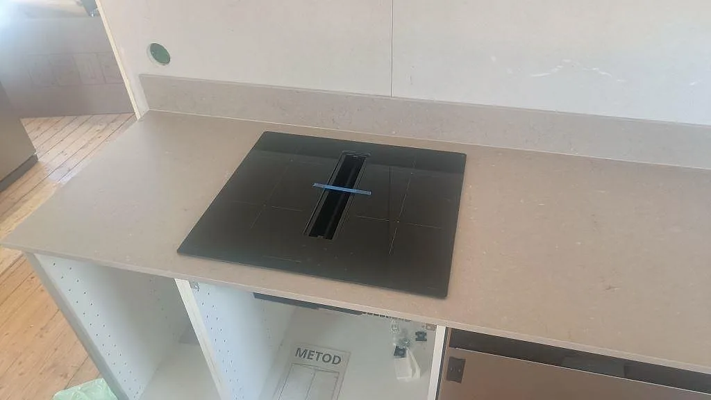 Svart häll i matt Silestone Coral Clay bänkskiva med låg stänkkant i ett kök under montering i Båstad.