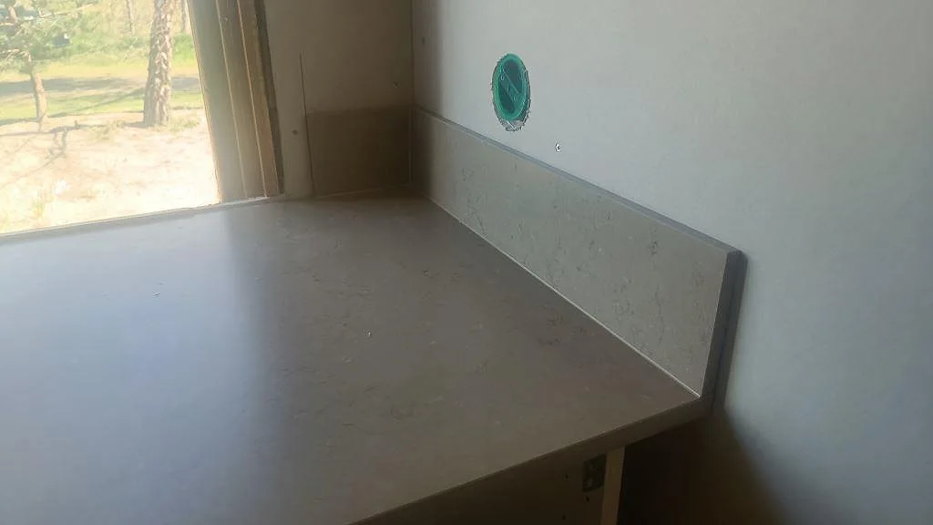 Matt Silestone Coral Clay bänkskiva under fönster med uppvikt stänkskydd i kök i Båstad.