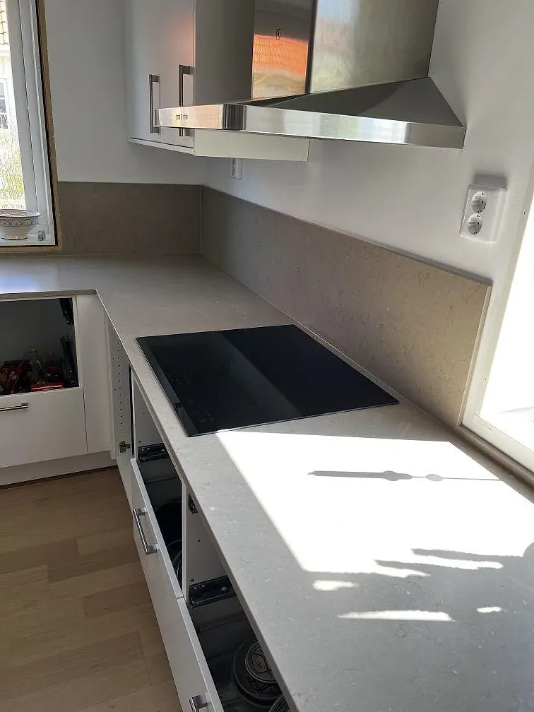 Infälld induktionshäll i köksbänkskiva av Silestone Coral Clay med rostfri köksfläkt i ett kök i Barsebäck.