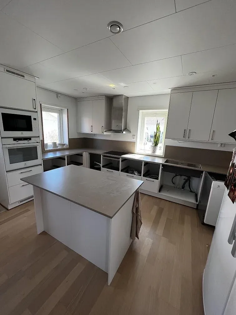 Kök med köksö och bänkskivor i Silestone Coral Clay, vita köksluckor och inbyggd ugn, fotograferat under montering i Barsebäck.