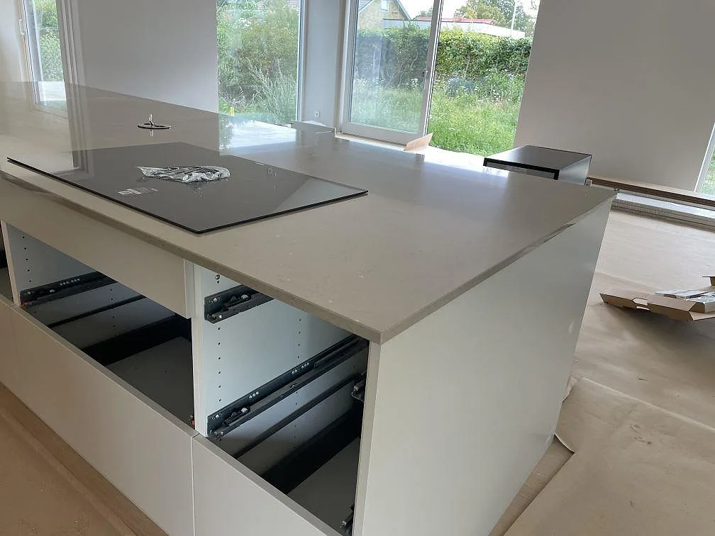 Ljus köksö i Silestone Coral Clay komposit med svart induktionshäll framför stora fönster i ett kök i Bjärred.