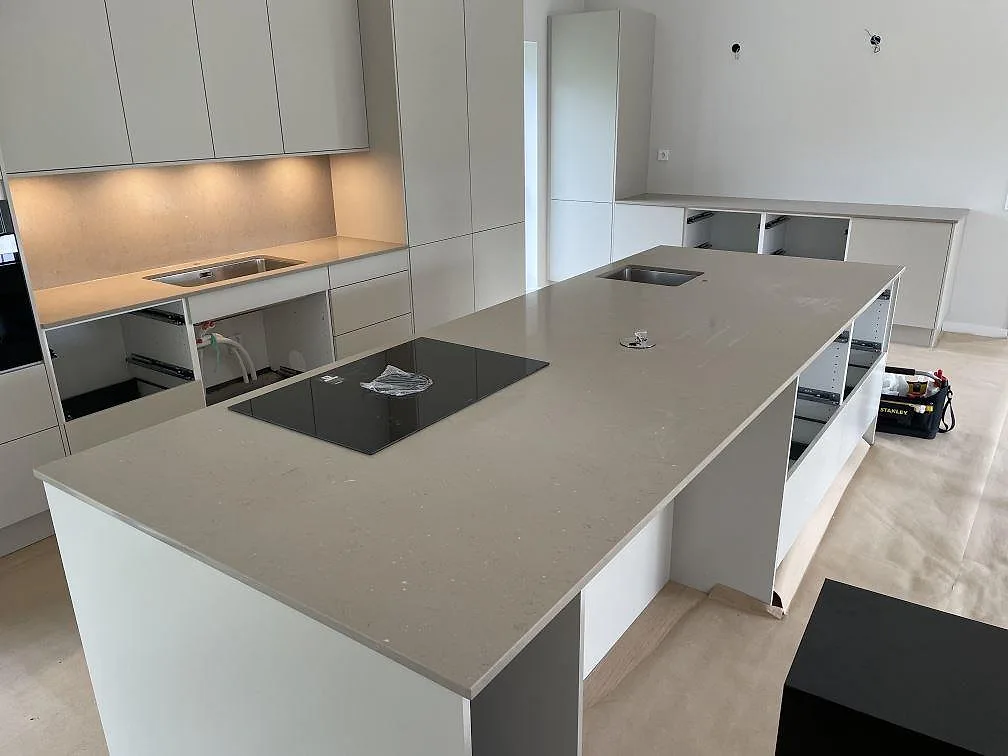 Stor köksö med köksbänkskiva i polerad Silestone Coral Clay komposit, svart induktionshäll och vit köksinredning i Bjärred.