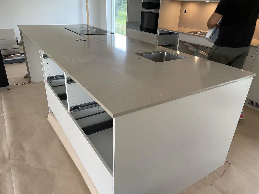 Köksö i polerad Silestone Coral Clay med rostfri underlimmad diskho, häll och vit modern inredning under montering i Bjärred.