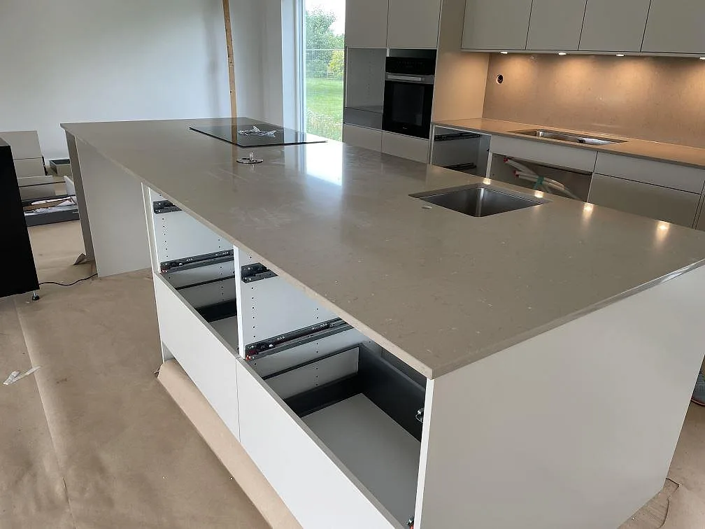 Polerad Silestone Coral Clay bänkskiva på ljus köksö med underlimmad rostfri diskho och svart häll i Bjärred.
