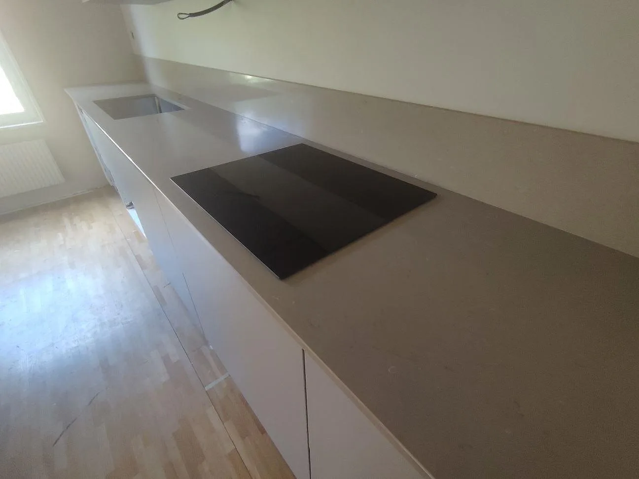 Rak köksbänk i polerad Silestone Coral Clay med svart häll, underlimmad diskho och låg stänkkant i ett kök i Björklinge.