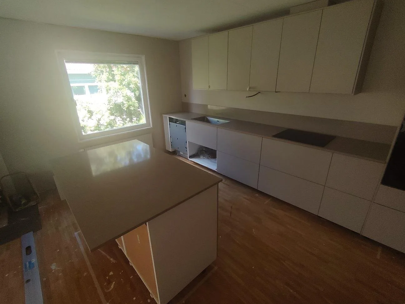 Kök i Björklinge med polerad Silestone Coral Clay som köksö, bänkskiva, stänkkant, svart häll och underlimmad rostfri diskho.