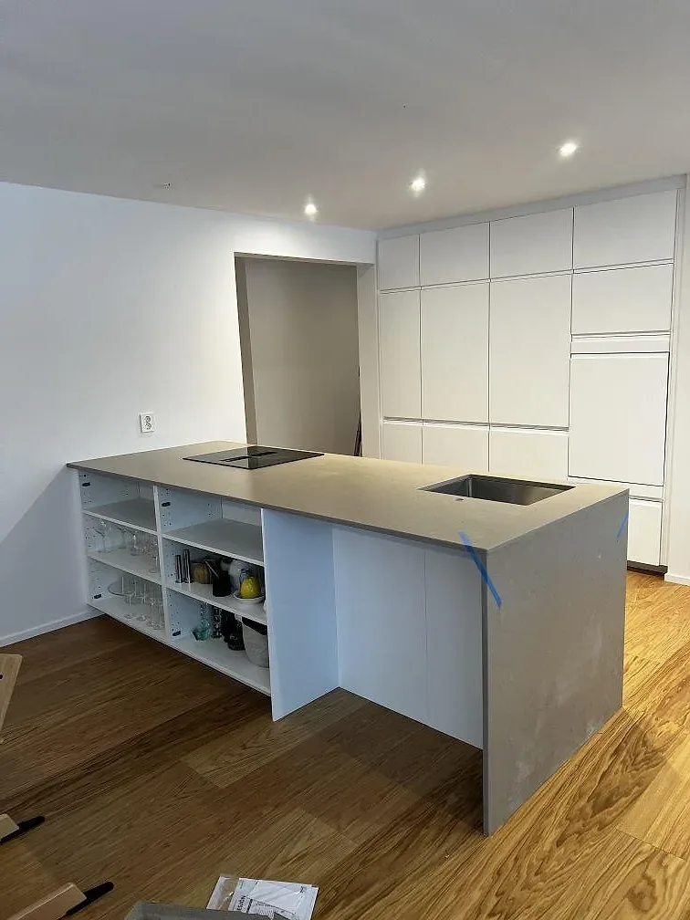 Köksö med bänkskiva i Silestone Coral Clay, matt Mocka, svart häll och öppna hyllfack i ett kök i Borås.