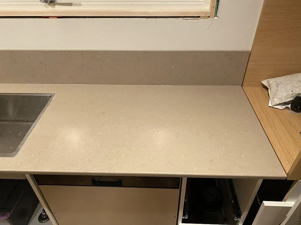 Arbetsyta under fönster i polerad Silestone Coral Clay med diskho och uppvikt stänkkant i ett kök i Borås.