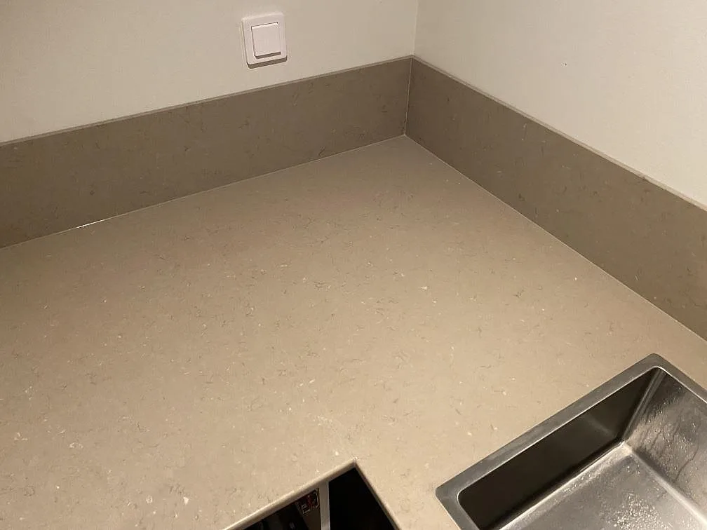 Hörnparti vid diskhon med polerad Silestone Coral Clay som köksbänkskiva och stänkkant mot ljus vägg i Borås.