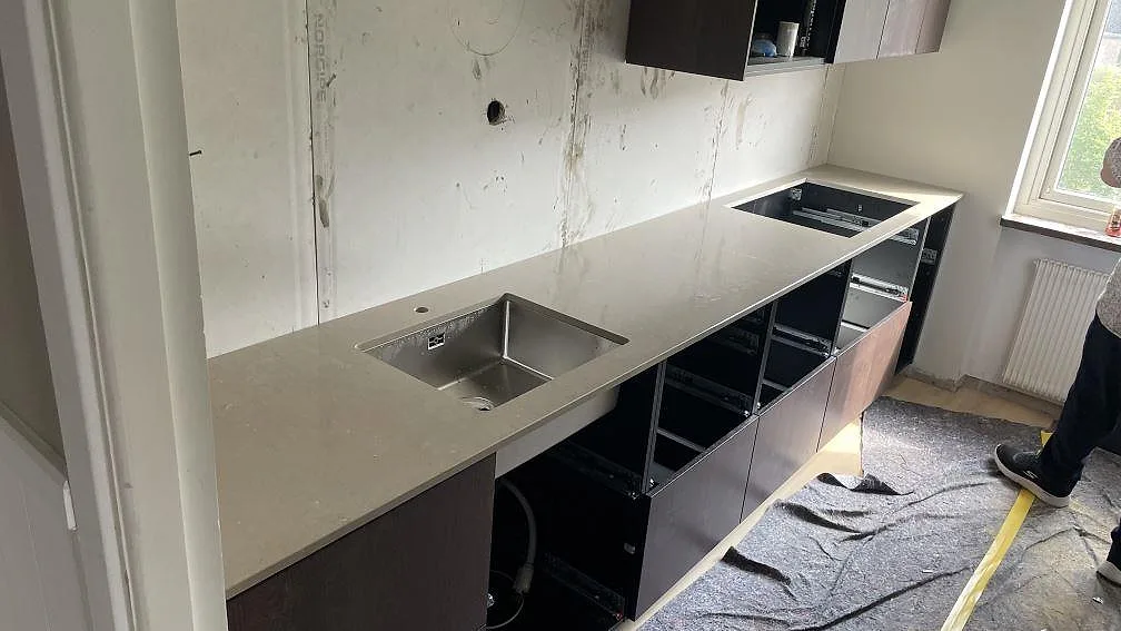 Köksbänkskiva i polerad Silestone Coral Clay, beigegrå kvartskomposit, med rostfri diskho och hällurtag under montering i Borås.