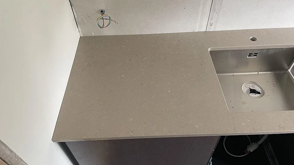 Detalj av vänster arbetsyta i polerad Silestone Coral Clay med diskret mönster och rostfri diskho i Borås.