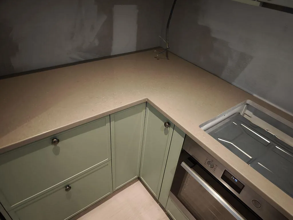 Hörn av köksbänkskiva i polerad Silestone Coral Clay med hällzon, ugn och gröna luckor i Dalby.