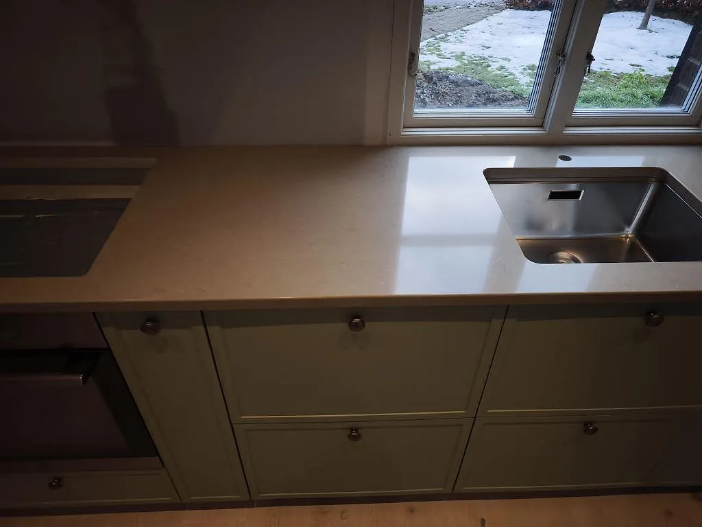Lång köksbänkskiva i polerad Silestone Coral Clay, 30 mm kvartskomposit, med rostfri diskho under fönster i Dalby.