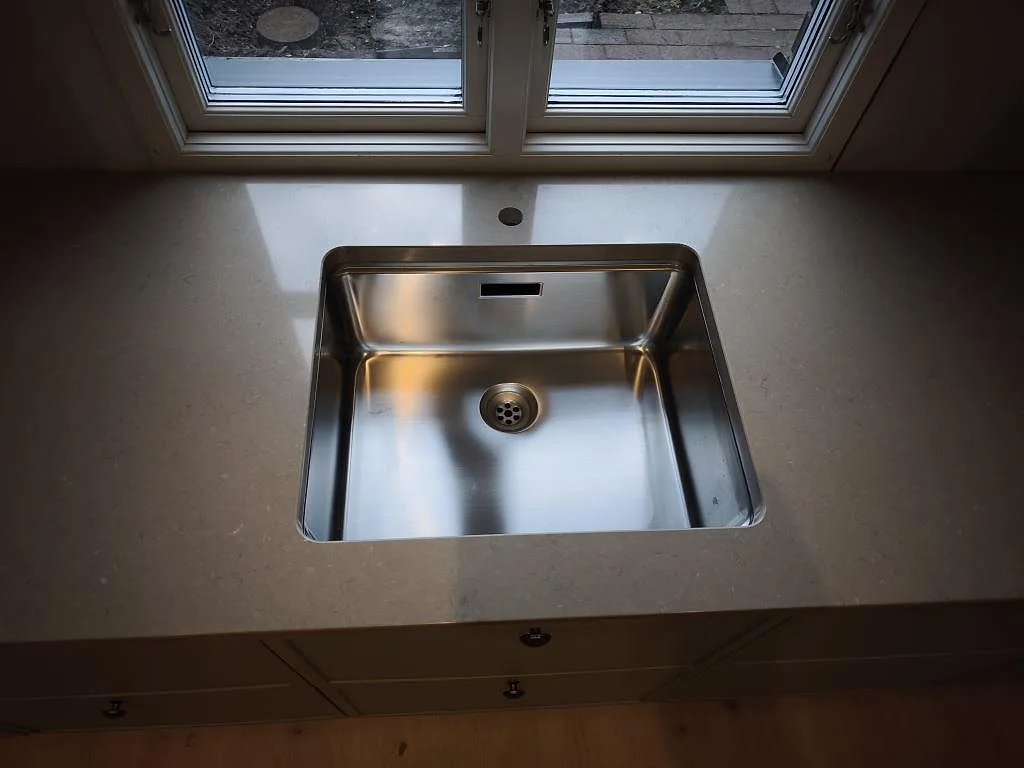 Detalj av rostfri diskho i polerad Silestone Coral Clay, 30 mm kvartskomposit, monterad vid fönster i Dalby.