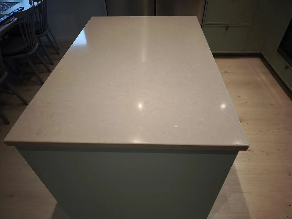 Närbild på köksö i polerad Silestone Coral Clay, 30 mm kvartskomposit, med ljusa reflexer och grön köksinredning i Dalby.