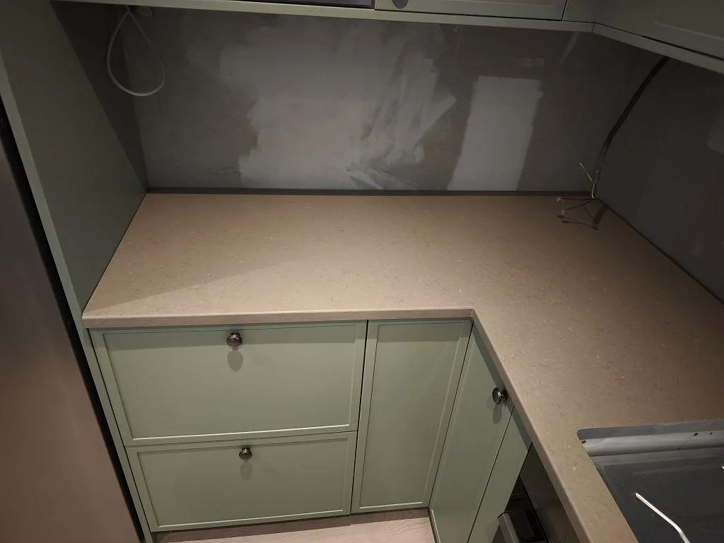 L-formad köksbänkskiva i polerad Silestone Coral Clay, 30 mm kvartskomposit, mot vägg under montering i Dalby.