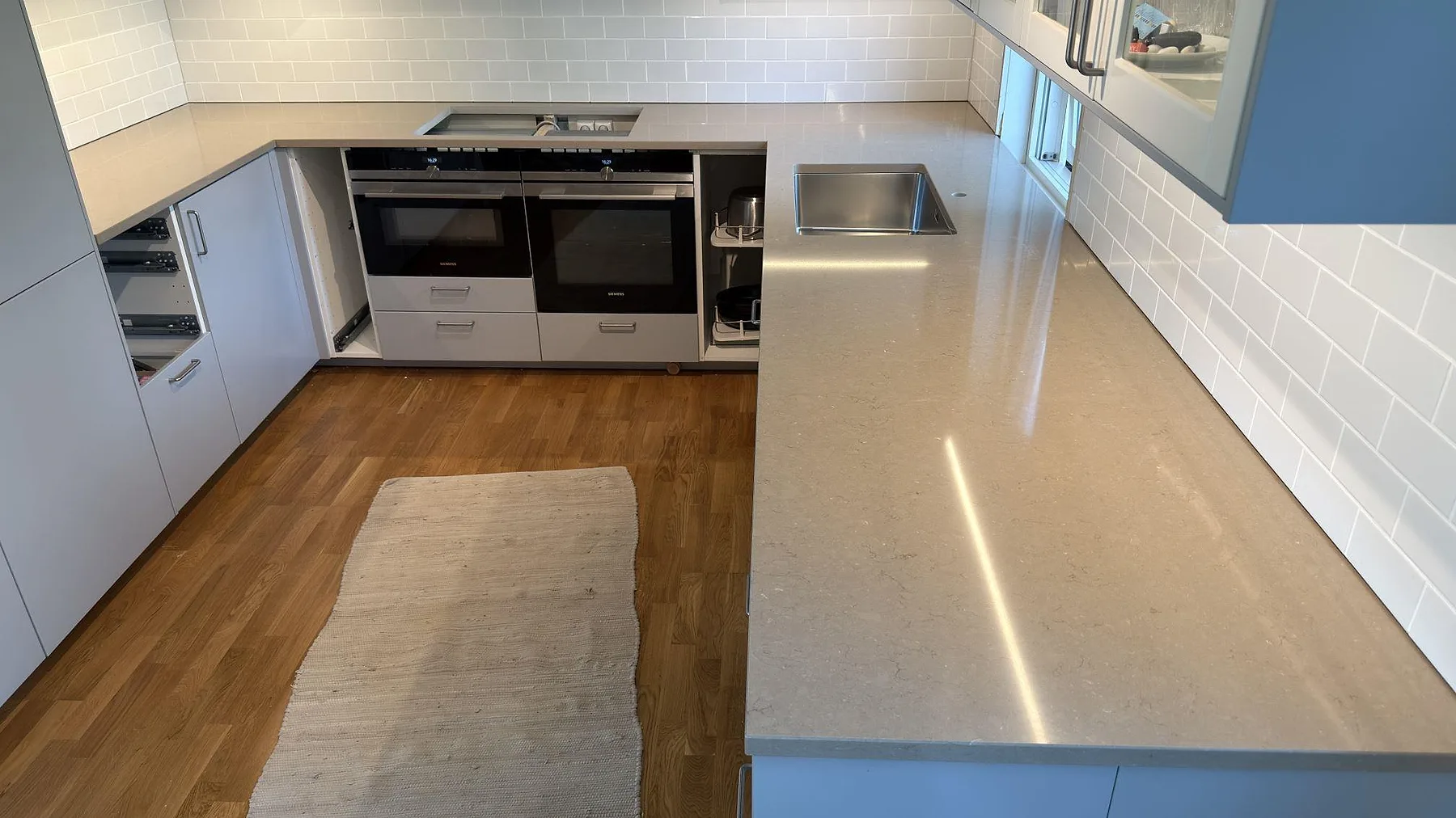 Närbild på polerad Silestone Coral Clay köksbänk med rostfri diskho, hälluttag och lång arbetsyta under väggskåp i Ekerö.