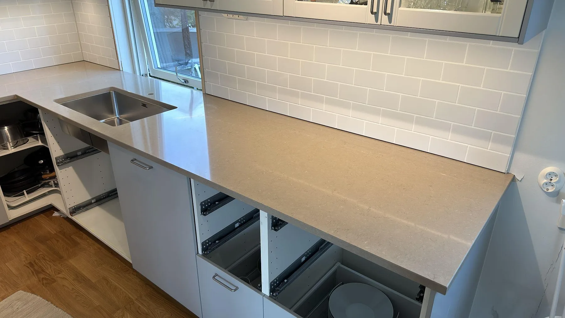 Detalj av Silestone Coral Clay köksbänkskiva, polerad, med rostfri diskho vid fönster och öppen lådstomme under montering i Ekerö.