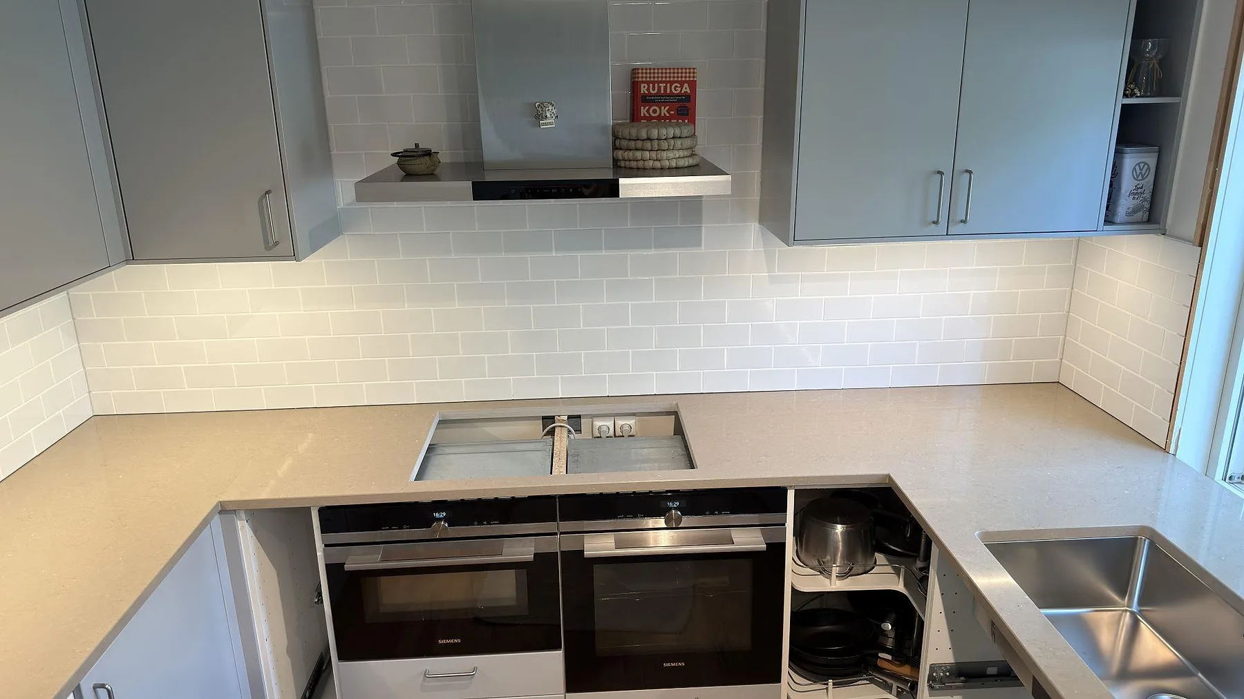 Polerad Silestone Coral Clay bänkskiva med öppning för häll, rostfri diskho och kaklad vägg i ett kök i Ekerö.