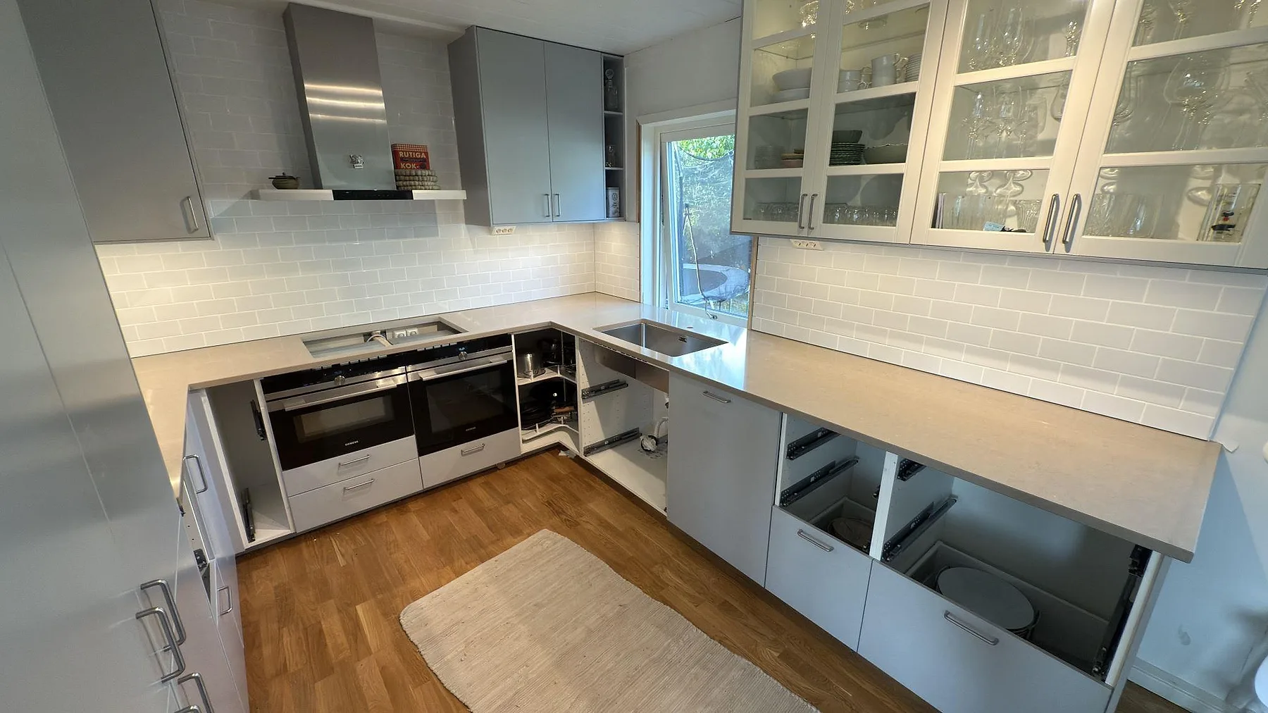 Köksbänkskiva i Silestone Coral Clay kvartskomposit, polerad 30 mm, som löper i L-form med rostfri diskho och hälluttag i ett kök i Ekerö.
