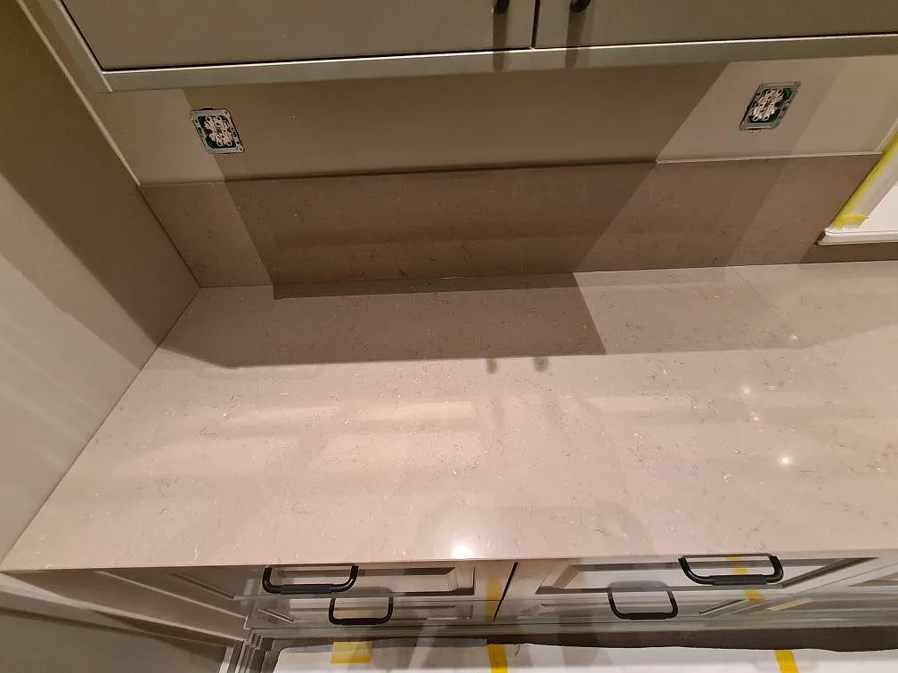 Väggbänk och stänkdetalj i polerad Silestone Coral Clay ovanför greige köksluckor i Enköping.