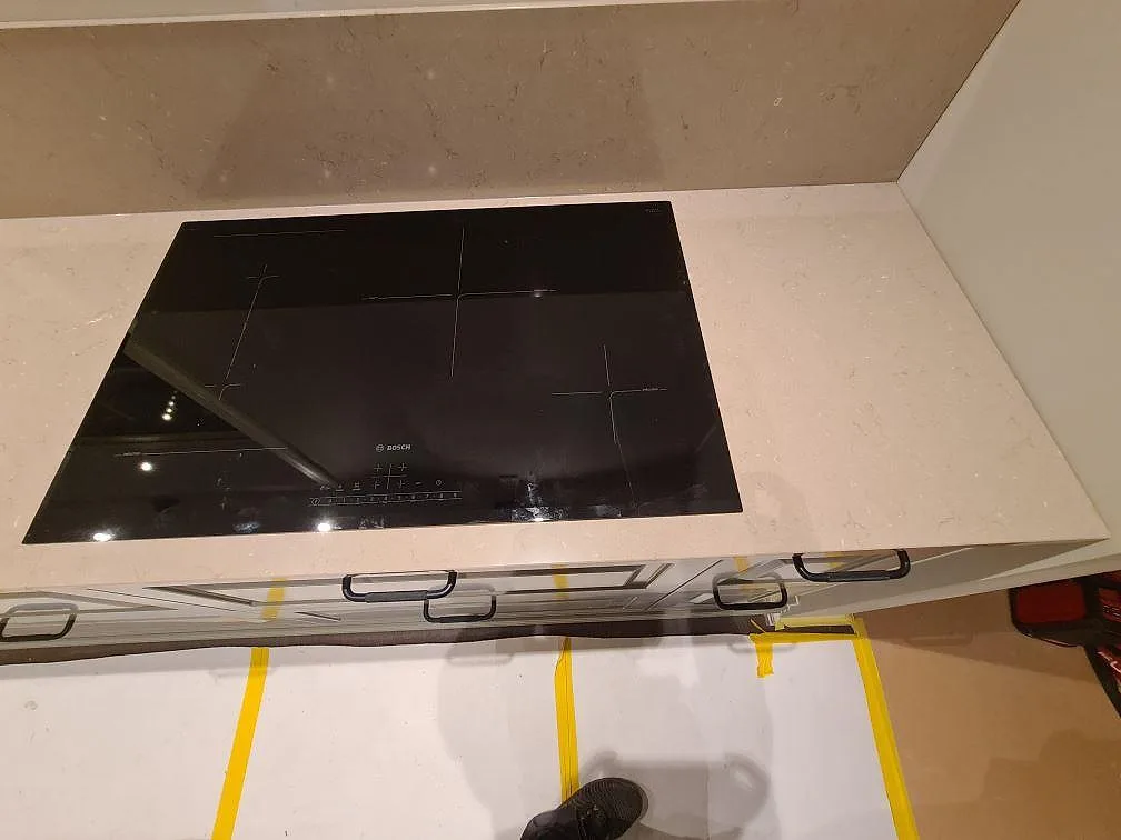 Svart induktionshäll infälld i polerad Silestone Coral Clay med matchande stänkkant i Enköping.