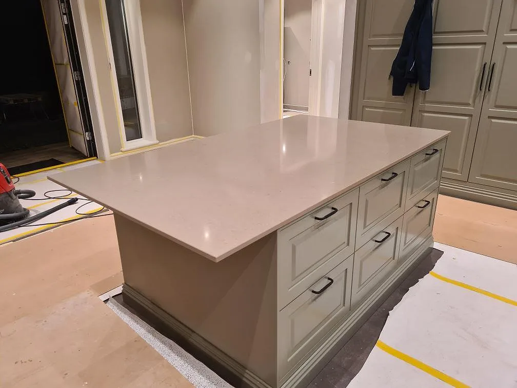 Stor köksö med bänkskiva i polerad Silestone Coral Clay på greige köksinredning under montering i Enköping.