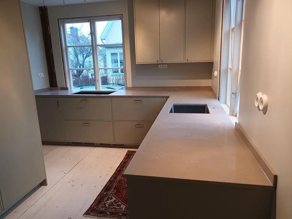 Köksbänkskiva i Silestone Coral Clay, matt Mocka-yta, U-formad bänk med urtag för diskho och häll och uppvikt stänkkant i ett kök under montering i Enskede.