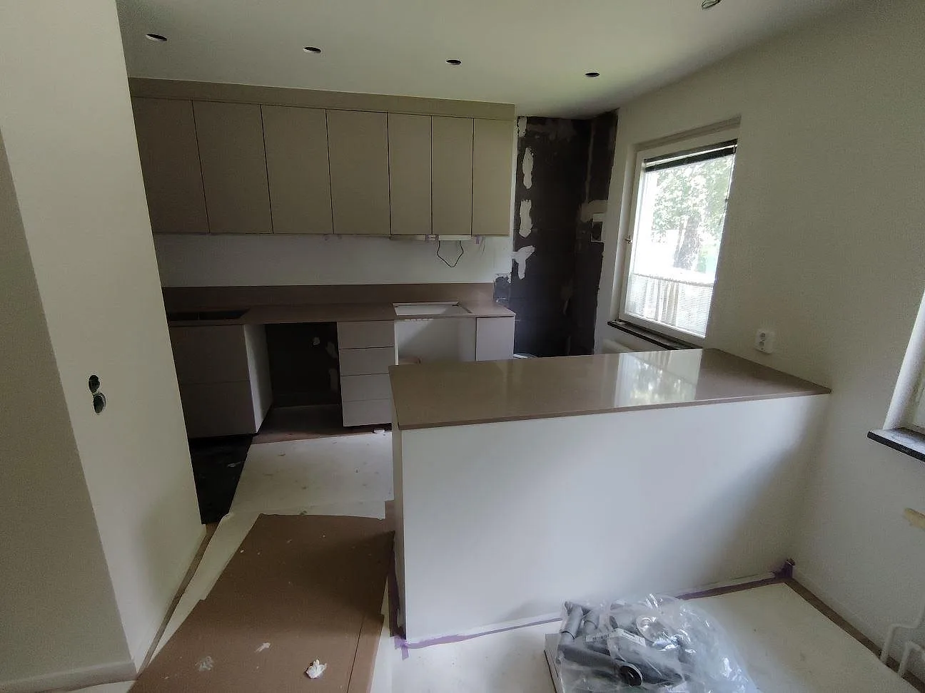 Köksbänkskiva i polerad Silestone Coral Clay, varm gråbeige kvartskomposit, monterad som peninsula i ett kök med greige stommar i Enskede.