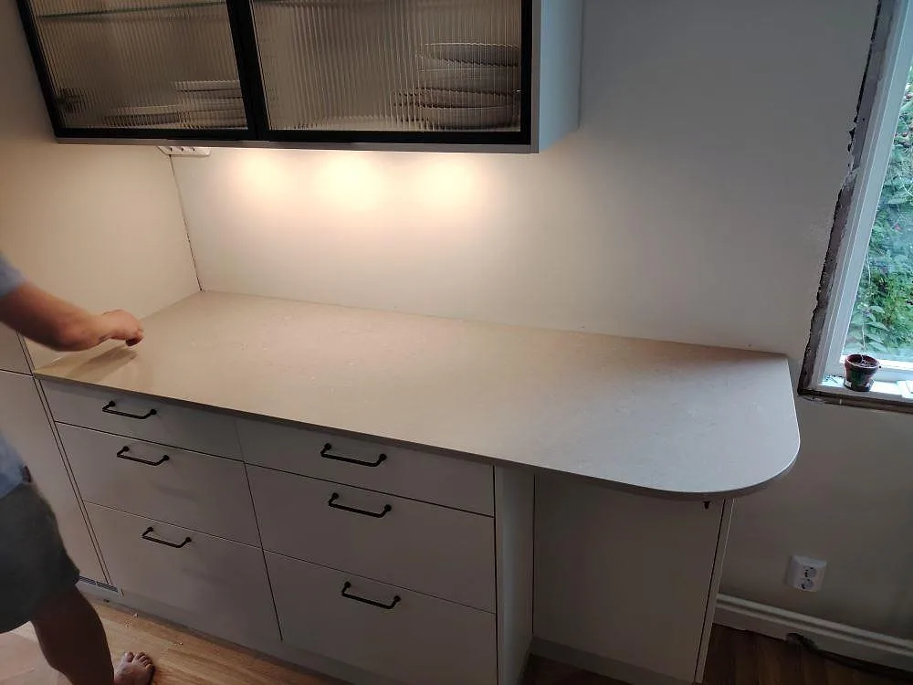Polerad Silestone Coral Clay-komposit som köksbänkskiva med rundad halvöände vid fönster i Enskede.