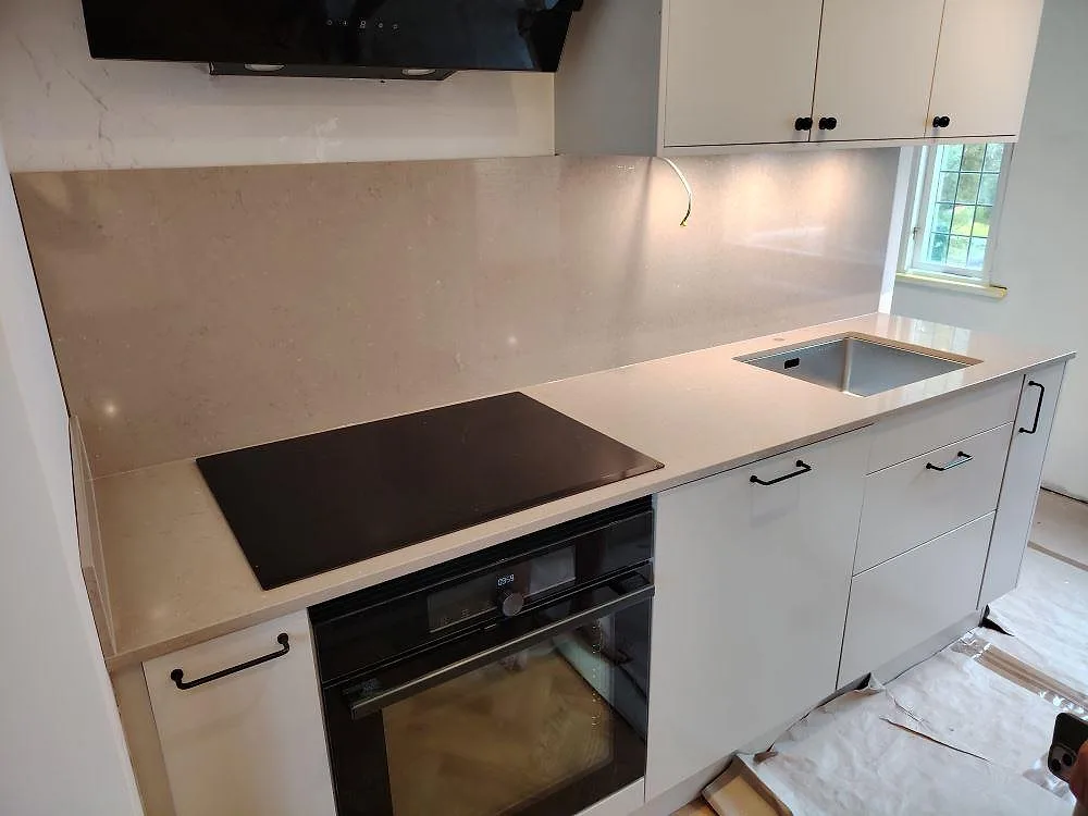 Köksbänkskiva i polerad Silestone Coral Clay-komposit med stänkskydd, induktionshäll och diskho i ett vitt kök i Enskede.