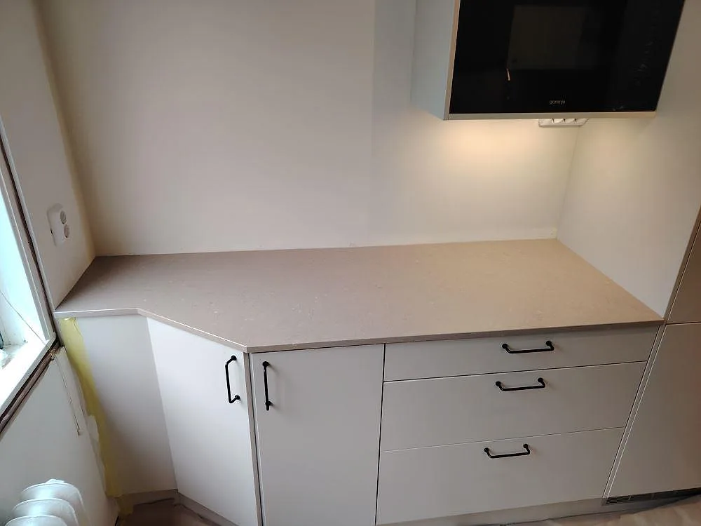 L-formad köksbänkskiva i polerad Silestone Coral Clay-komposit med låg stänkkant och vit skåpsinredning i Enskede.