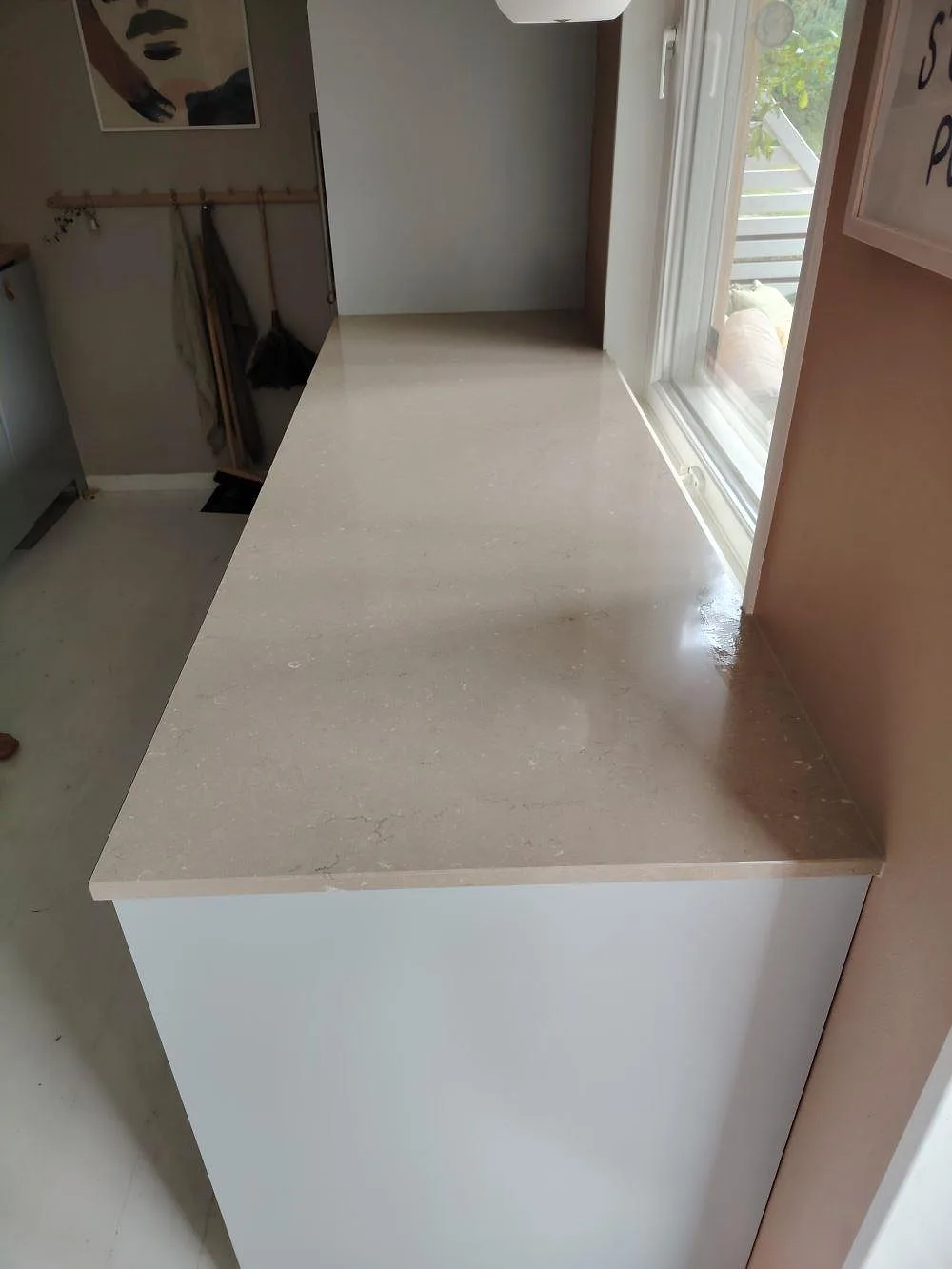 Polerad köksbänkskiva i Silestone Coral Clay, 20 mm kvartskomposit, som smal halvö vid ett fönster i ett kök i Enskede.