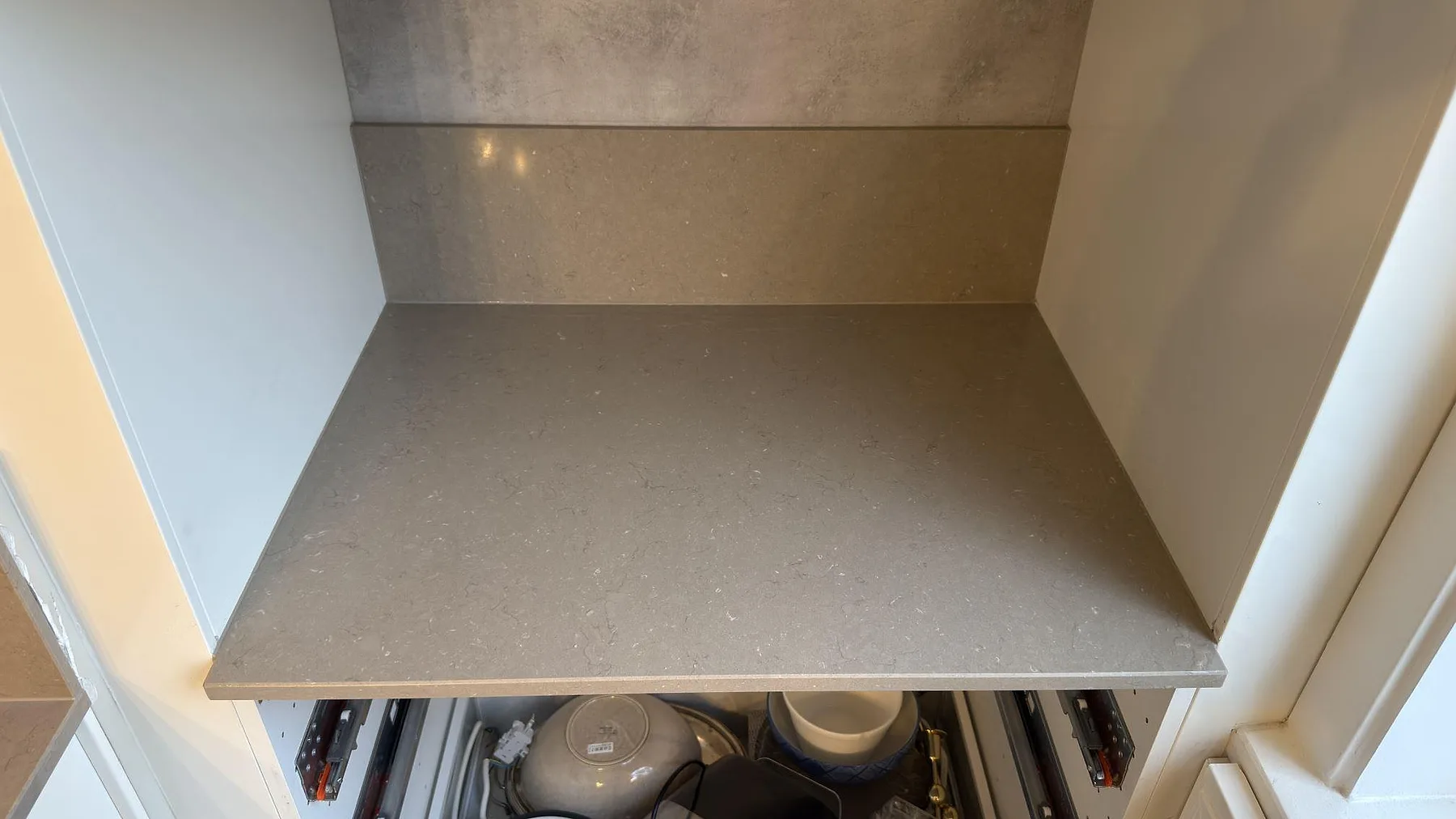 Sidobänk i polerad Silestone Coral Clay komposit med matchande stänkskydd i ett kök under montering i Enskede.