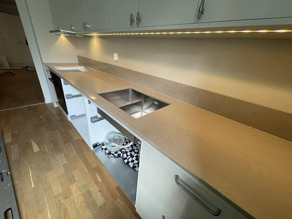 Lång köksbänkskiva i polerad Silestone Coral Clay med rostfri diskho och låg stänkkant under väggskåp i Enskededalen.