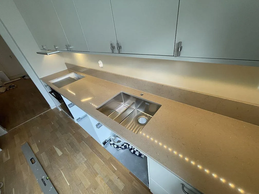 Detalj av polerad Silestone Coral Clay i kök, med rostfri diskho, hällöppning och låg stänkkant i Enskededalen.