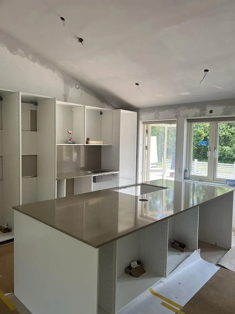 Köksö och bänkskiva i polerad Silestone Coral Clay komposit under montering i ett ljust kök i Färjestaden.