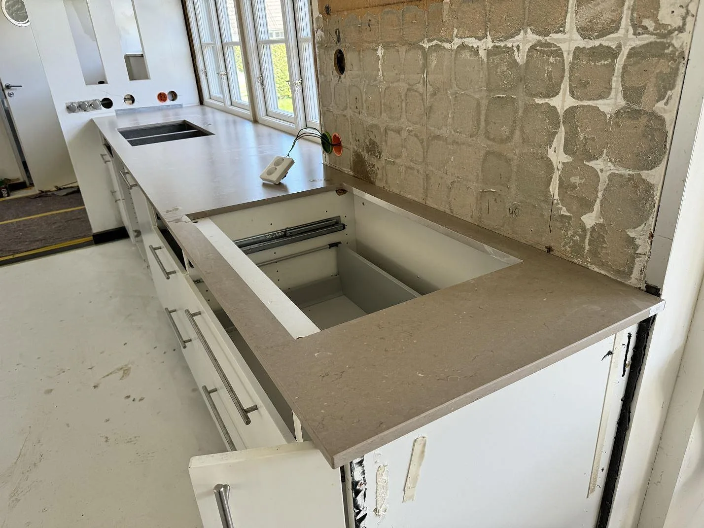 Silestone Coral Clay som matt köksbänkskiva med hällurskärning, dubbelho och exponerad vägg under montering i Falsterbo.