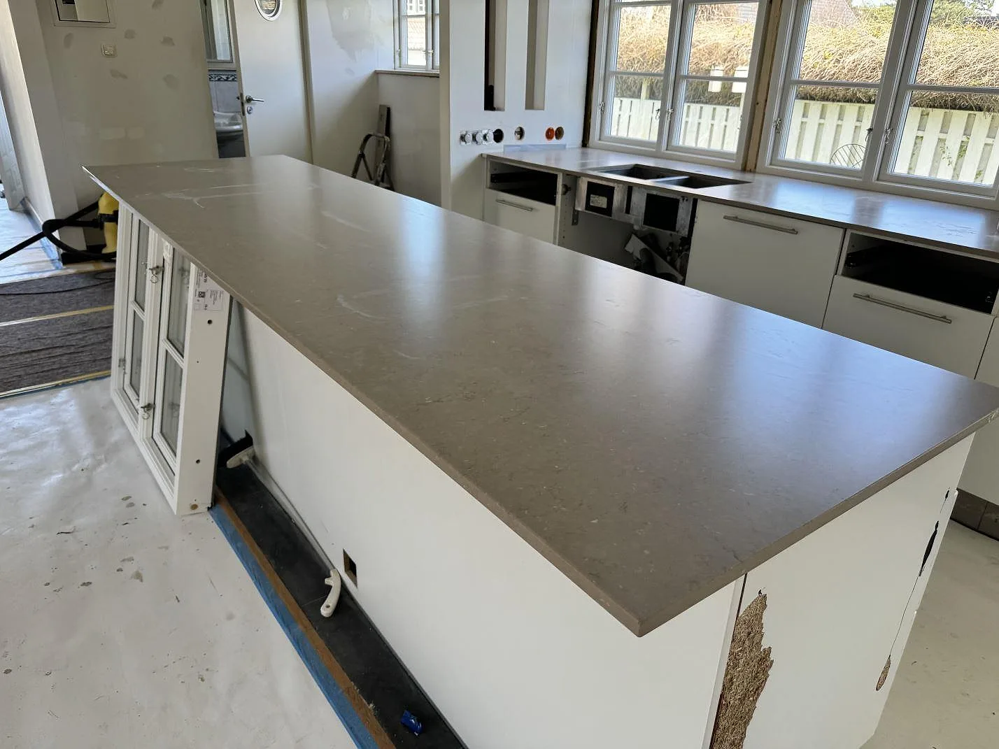 Köksö i Silestone Coral Clay med matt Mocka-yta framför fönsterrad och diskbänk i Falsterbo.