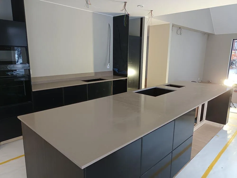 Köksö och perimeterbänk i polerad Silestone Coral Clay med urtag för häll, sett från andra hållet i ett kök under montering i Falun.