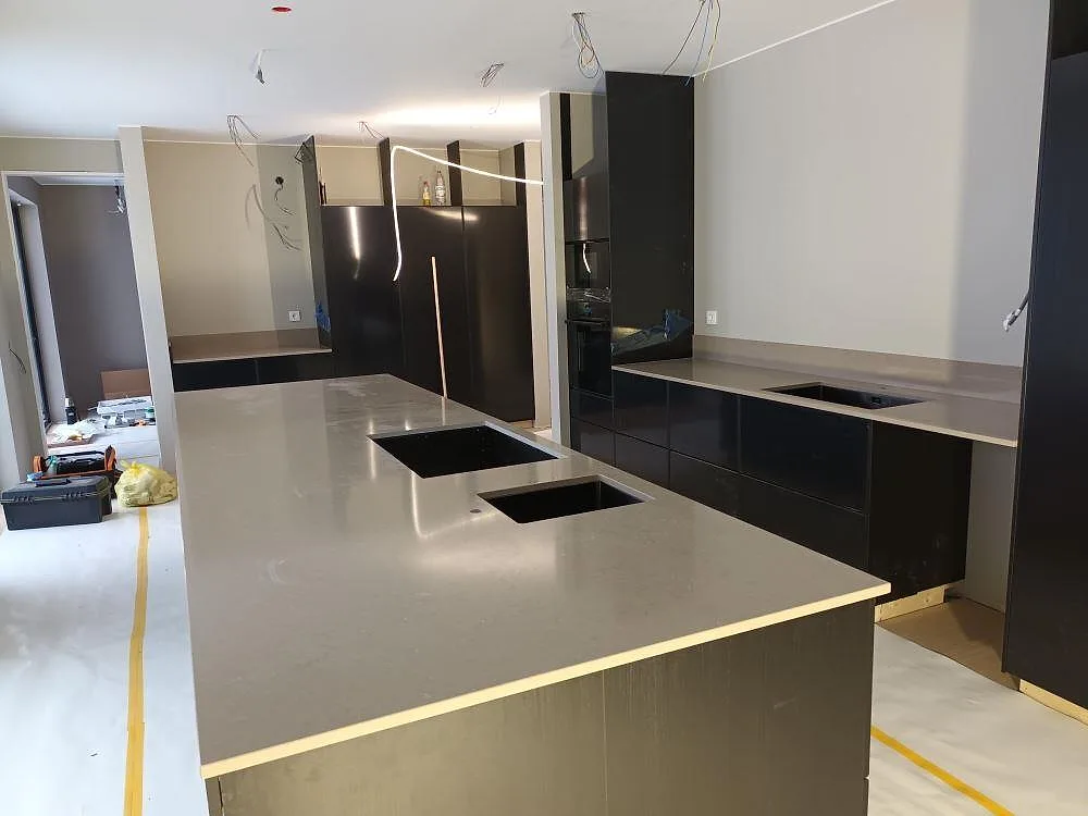 Köksbänkskiva i Silestone Coral Clay, polerad varm greige kvartskomposit, på en stor köksö med två underlimmade hoar i ett kök under montering i Falun.